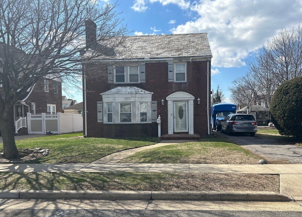 view of front of house featuring a chimney, fence, brick siding, aphalt driveway, and a front lawn