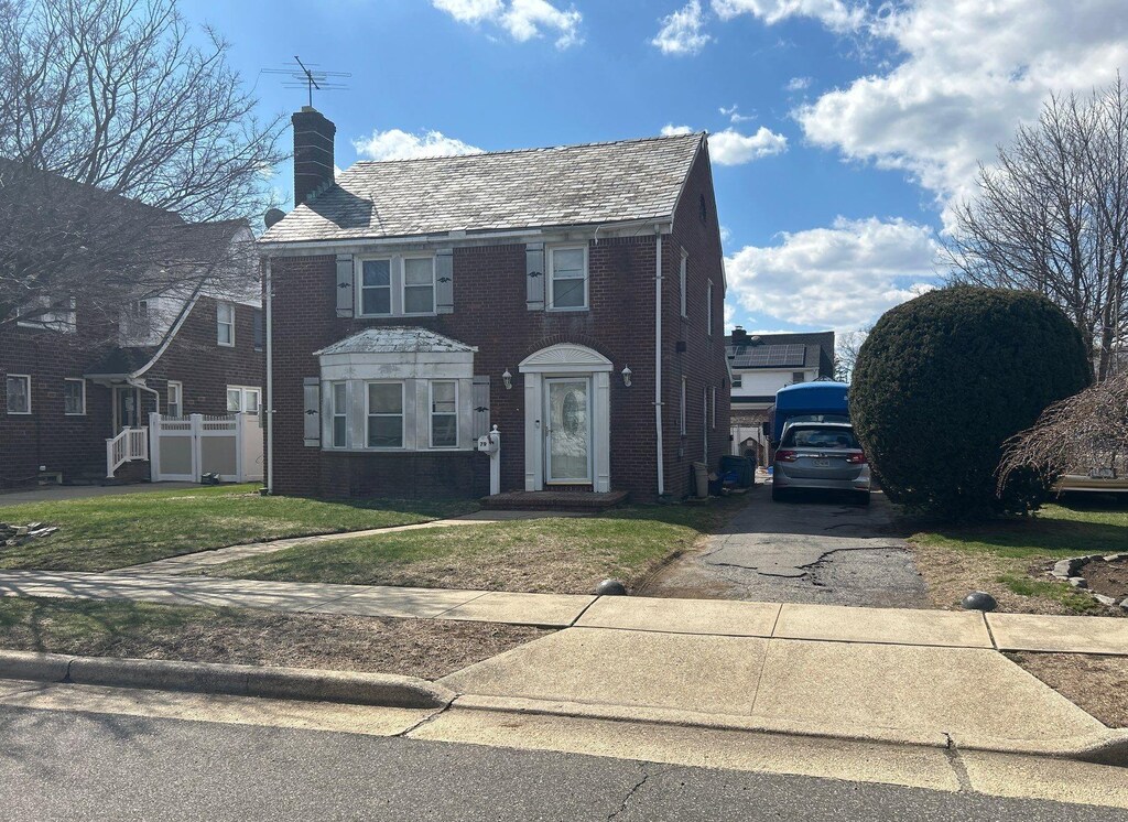 view of front facade with brick siding, a front yard, driveway, and a chimney