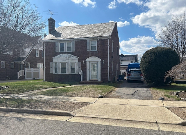 view of front facade with brick siding, a front yard, driveway, and a chimney