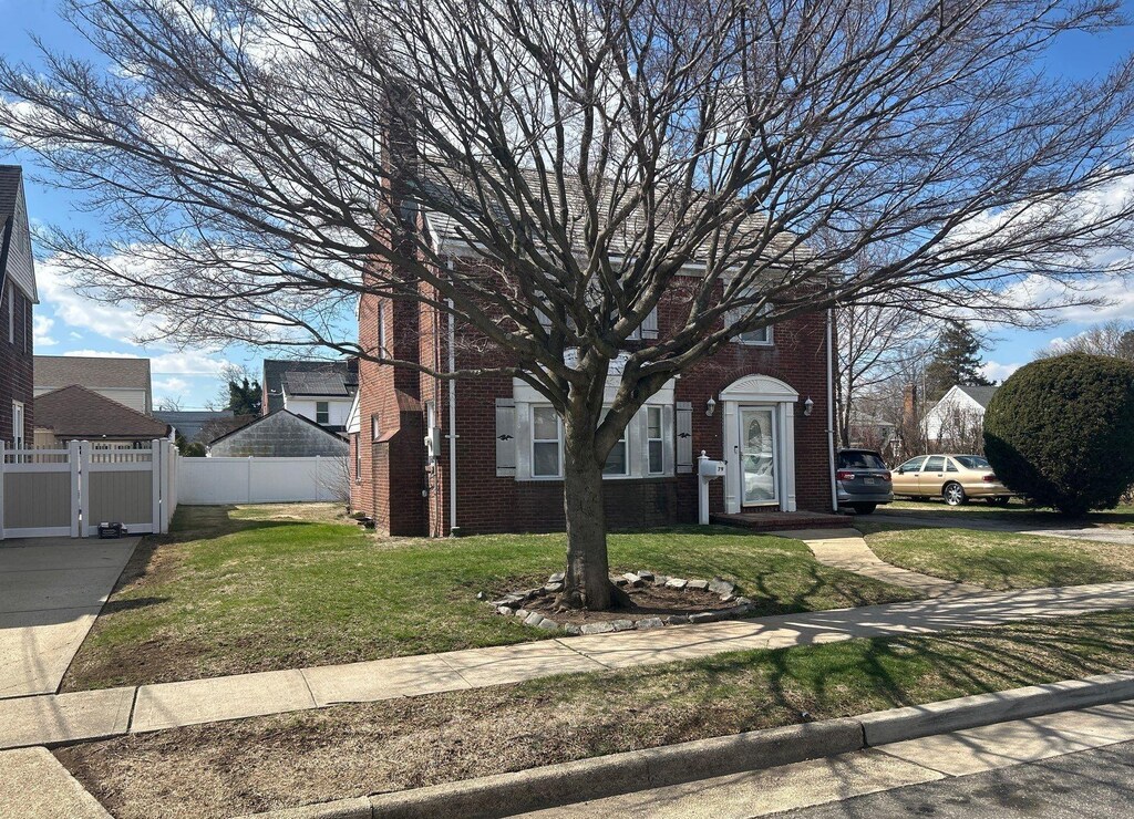 view of property hidden behind natural elements with a front yard, fence, and brick siding