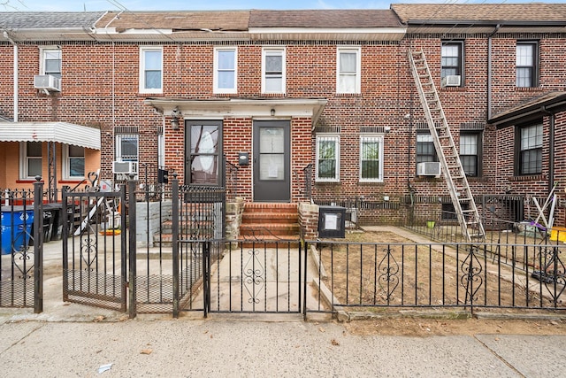 townhome / multi-family property featuring brick siding, a fenced front yard, roof with shingles, and entry steps