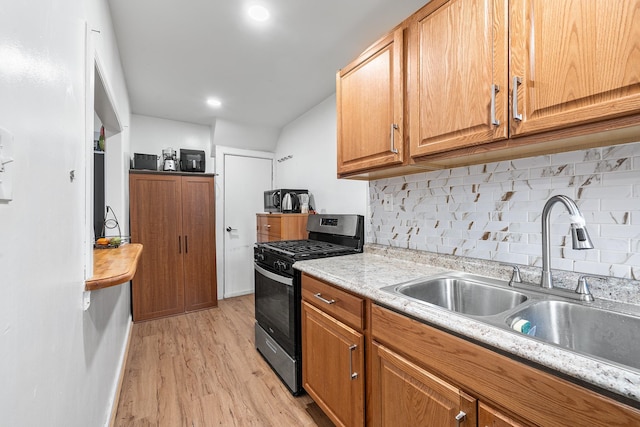 kitchen with light countertops, stainless steel gas stove, backsplash, a sink, and light wood-style floors