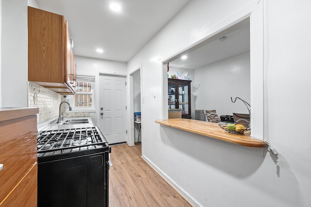 kitchen featuring black gas range oven, brown cabinets, a sink, light wood-type flooring, and backsplash