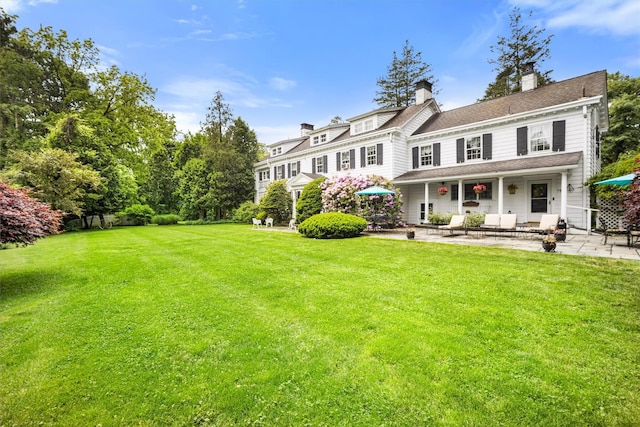 rear view of property featuring a chimney, roof with shingles, a patio, and a yard