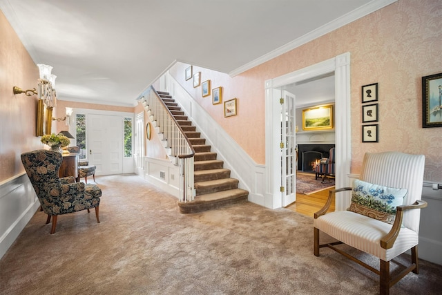living area featuring wallpapered walls, crown molding, stairway, and wainscoting