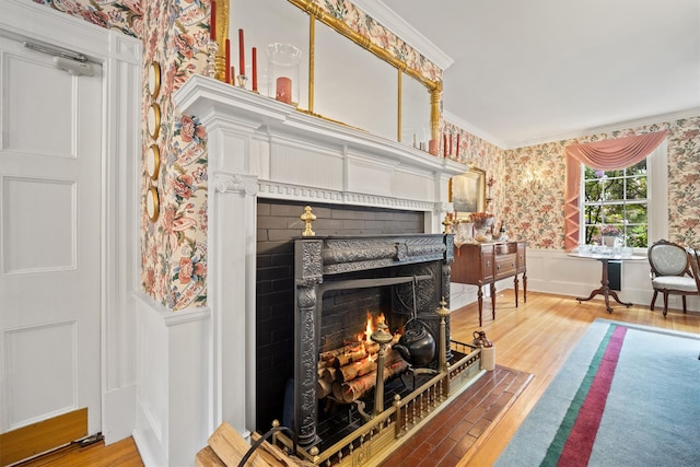 living room featuring a fireplace with flush hearth, ornamental molding, wallpapered walls, wood finished floors, and wainscoting