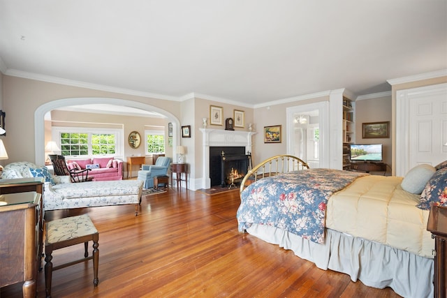 bedroom with arched walkways, a fireplace with flush hearth, crown molding, and wood finished floors