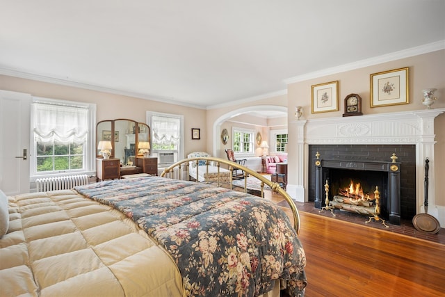 bedroom featuring ornamental molding, radiator, arched walkways, and wood finished floors