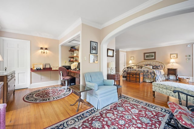 bedroom with arched walkways, built in desk, crown molding, and hardwood / wood-style flooring