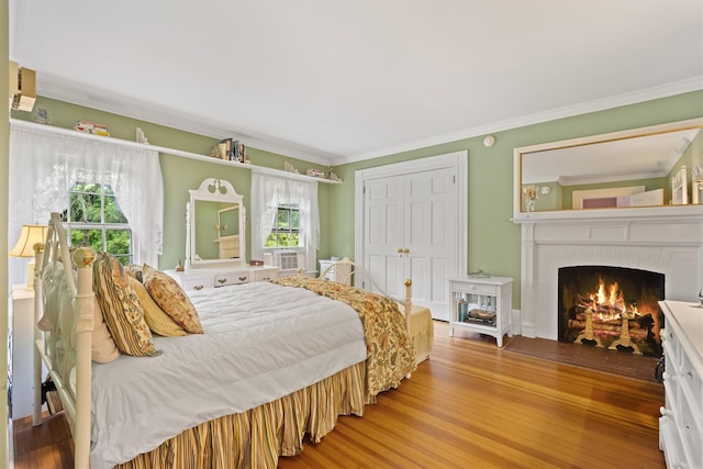 bedroom with a closet, a fireplace, wood finished floors, and crown molding