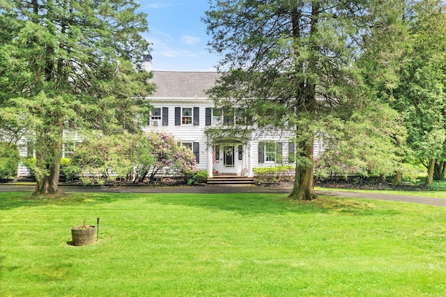 colonial inspired home featuring a chimney, a front lawn, and roof with shingles