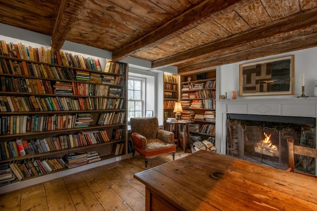 sitting room with a warm lit fireplace, wood ceiling, beamed ceiling, bookshelves, and wood-type flooring