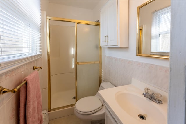 full bathroom featuring a shower stall, toilet, vanity, tile walls, and wainscoting