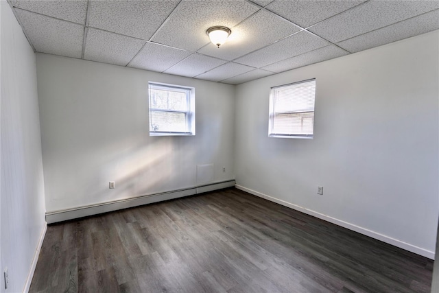 empty room with a baseboard radiator, a drop ceiling, baseboards, and dark wood-style flooring