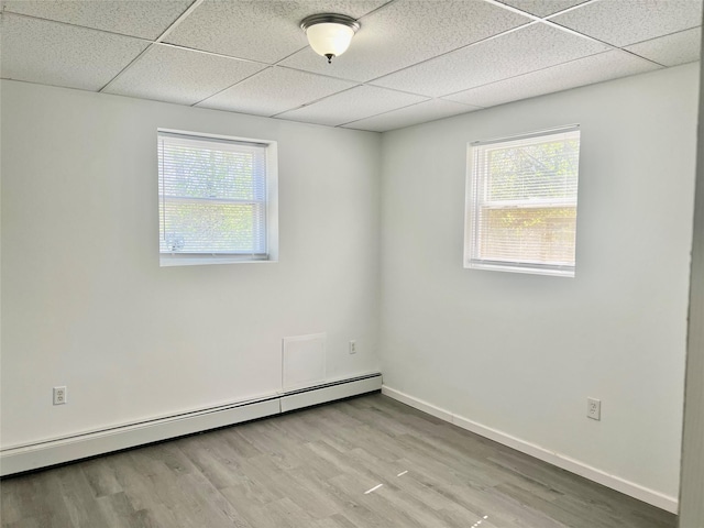 unfurnished room featuring a baseboard heating unit, a healthy amount of sunlight, and wood finished floors