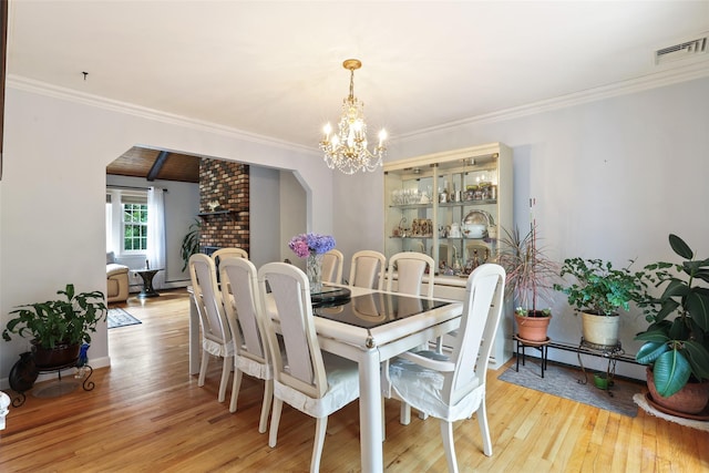 dining room with light wood-style floors, visible vents, crown molding, arched walkways, and an inviting chandelier