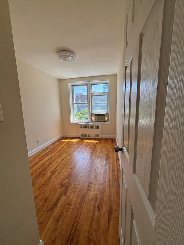 unfurnished room featuring radiator heating unit, hardwood / wood-style floors, baseboards, and cooling unit