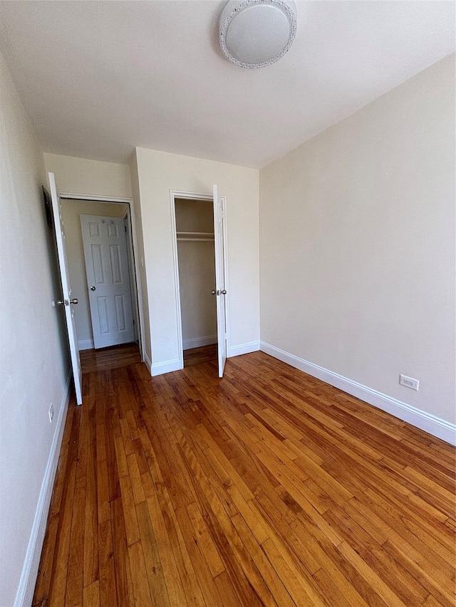 unfurnished bedroom featuring wood-type flooring, baseboards, and a closet