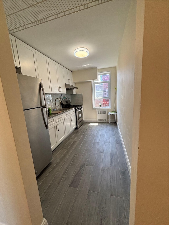 kitchen featuring appliances with stainless steel finishes, dark wood-type flooring, white cabinets, under cabinet range hood, and tasteful backsplash