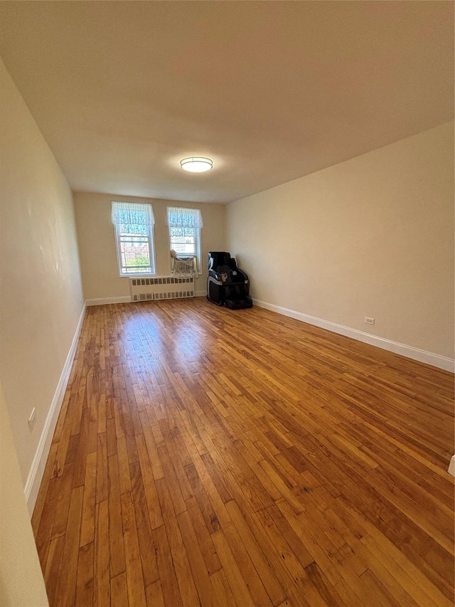 spare room with wood-type flooring, baseboards, and radiator