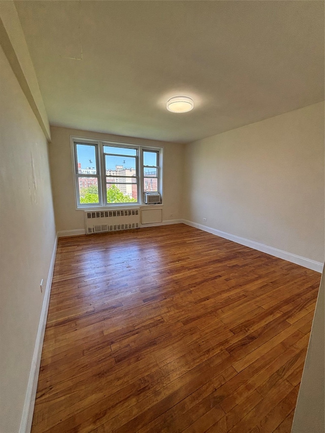 empty room featuring radiator, wood-type flooring, and baseboards