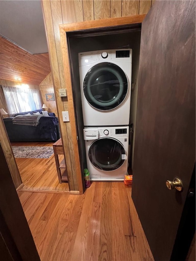 laundry room with wood finished floors, stacked washer / drying machine, and wood walls