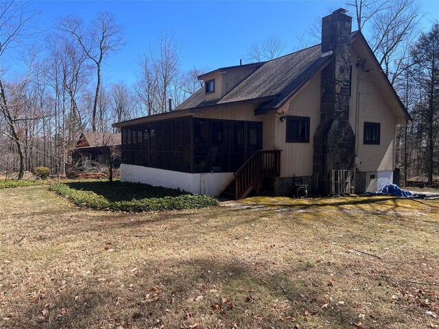 view of side of home with a yard, a sunroom, roof with shingles, and a chimney