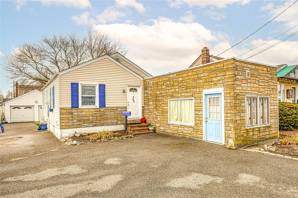 644 Merrick Rd, Copiague, NY 11726 - view of front of home featuring aphalt driveway, a detached garage, an outdoor structure, stone siding, and a chimney