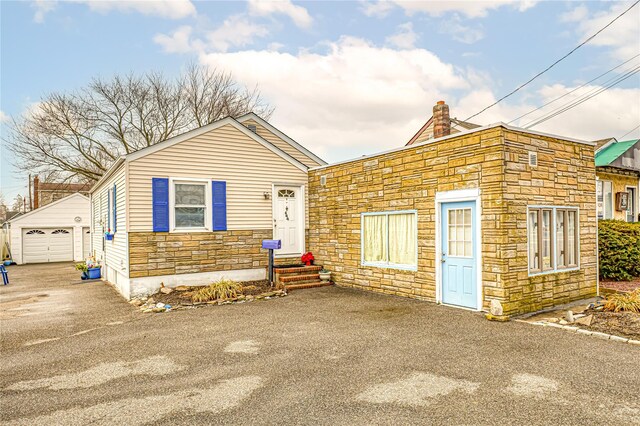 644 Merrick Rd, Copiague, NY 11726 - view of front of home featuring aphalt driveway, a detached garage, an outdoor structure, stone siding, and a chimney