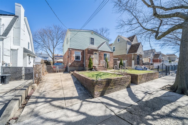 view of front of property featuring driveway, a gate, fence, brick siding, and a residential view