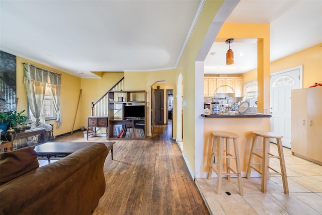living area featuring arched walkways, baseboards, stairway, and light wood finished floors