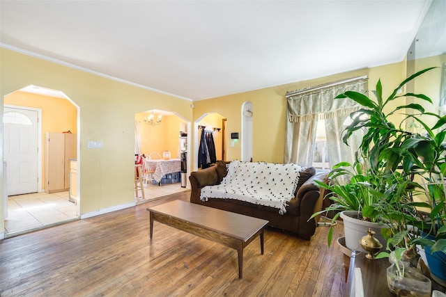 living area with arched walkways, crown molding, a chandelier, and wood finished floors