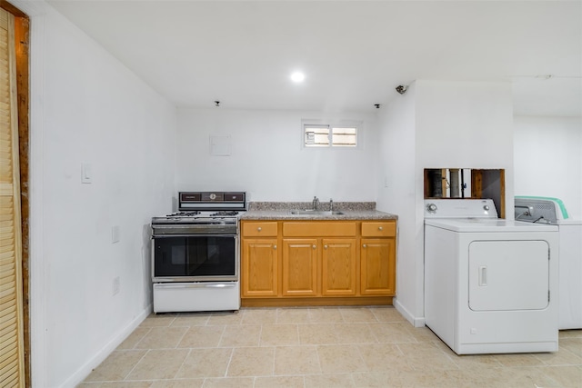 kitchen with white gas range oven, a sink, separate washer and dryer, brown cabinetry, and baseboards