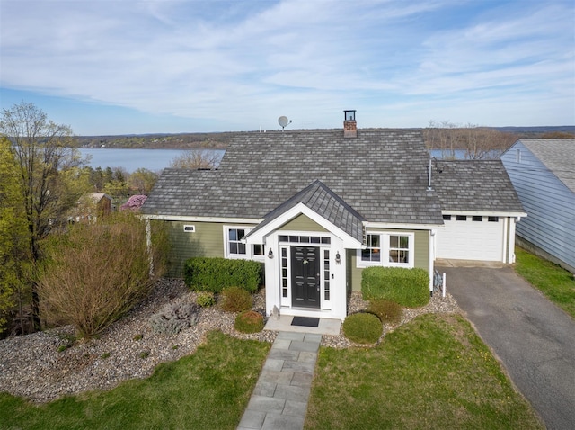 view of front of house featuring roof with shingles, a water view, driveway, a chimney, and a garage