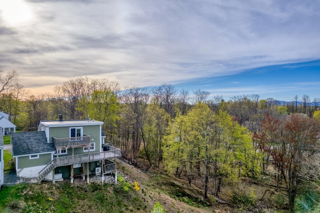 rear view of property featuring stairs, a wooded view, and a deck
