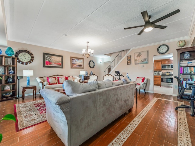 living area featuring ceiling fan with notable chandelier, dark wood finished floors, ornamental molding, stairs, and baseboards