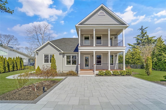 neoclassical / greek revival house with fence, a balcony, a front yard, covered porch, and a shingled roof