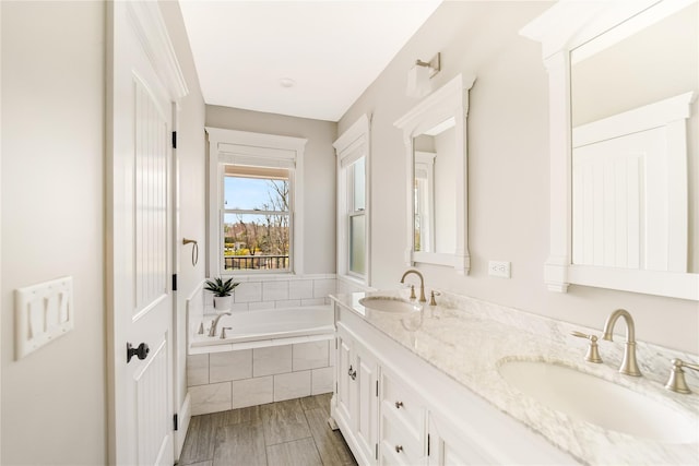 bathroom featuring double vanity, a bath, wood finished floors, and a sink
