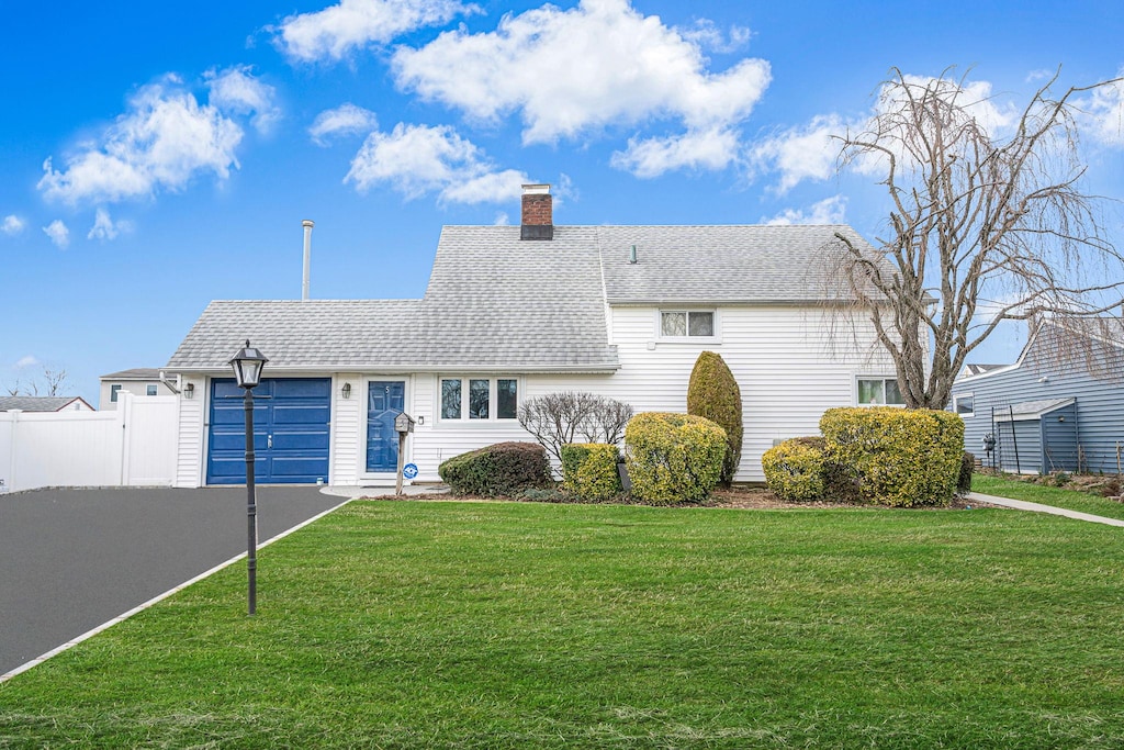 view of front of house featuring roof with shingles, a chimney, fence, and a front lawn
