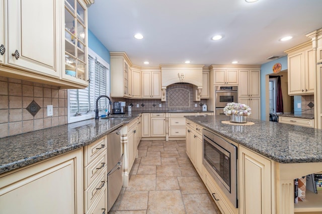 kitchen featuring cream cabinets, appliances with stainless steel finishes, a sink, stone finish flooring, and a kitchen island