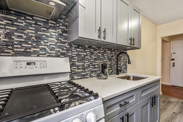 kitchen with white gas stove, a sink, ventilation hood, gray cabinetry, and tasteful backsplash