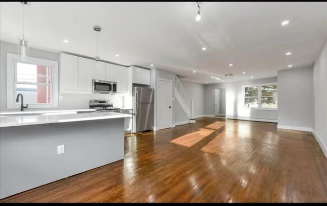 kitchen featuring dark wood-style flooring, white cabinets, light countertops, stainless steel appliances, and pendant lighting