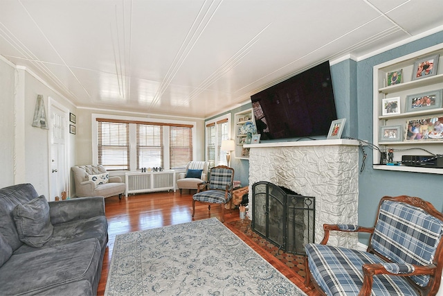 living area featuring hardwood / wood-style floors, radiator heating unit, crown molding, and a stone fireplace