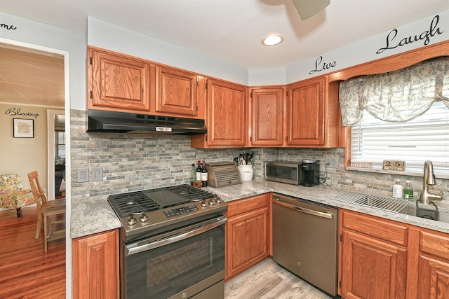 kitchen with tasteful backsplash, appliances with stainless steel finishes, under cabinet range hood, ceiling fan, and a sink