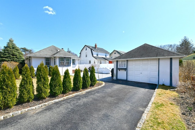 view of front of property with aphalt driveway, stucco siding, an outdoor structure, and fence