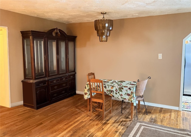 dining room with a notable chandelier, a textured ceiling, baseboards, and wood finished floors
