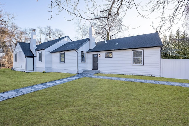 view of front of home with a chimney, roof with shingles, fence, and a front lawn