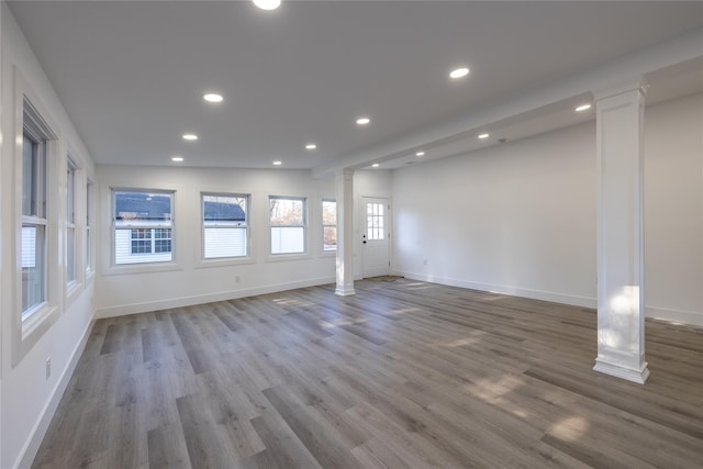 unfurnished living room with decorative columns, wood finished floors, baseboards, and recessed lighting