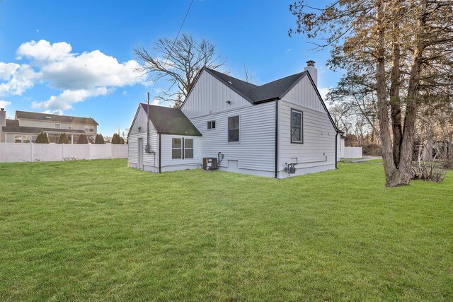back of property with cooling unit, a chimney, fence, board and batten siding, and a lawn