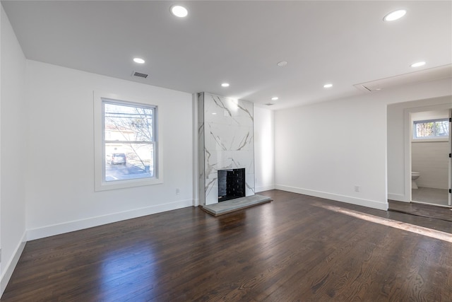 unfurnished living room with dark wood-type flooring, visible vents, a high end fireplace, and recessed lighting
